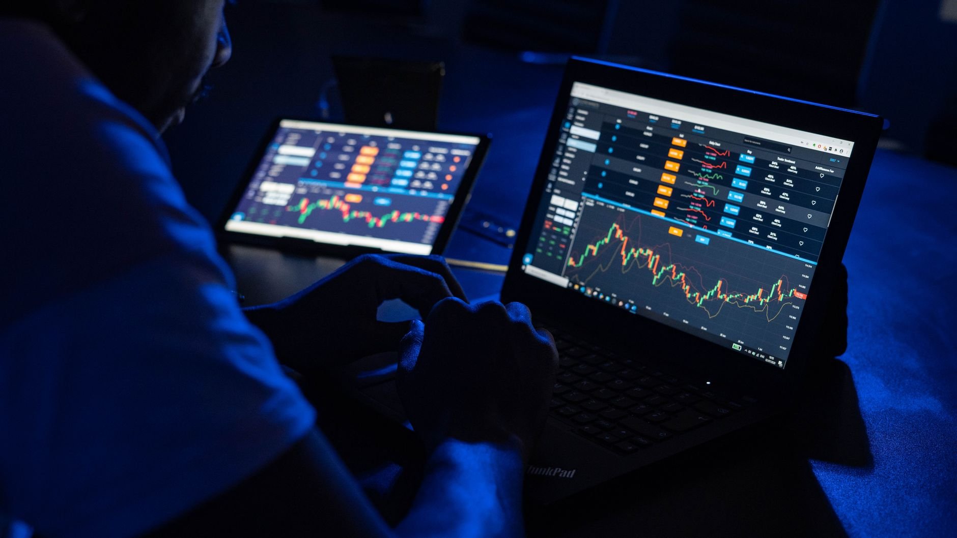 Man analysing financial charts and data on laptops in a dimly lit room.